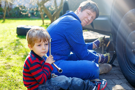 2岁的小金发孩子和他父亲用充气扳手换车轮图片