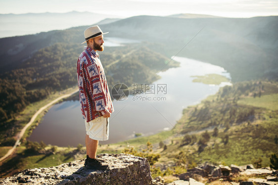 戴帽子的人站在有湖的山顶上图片