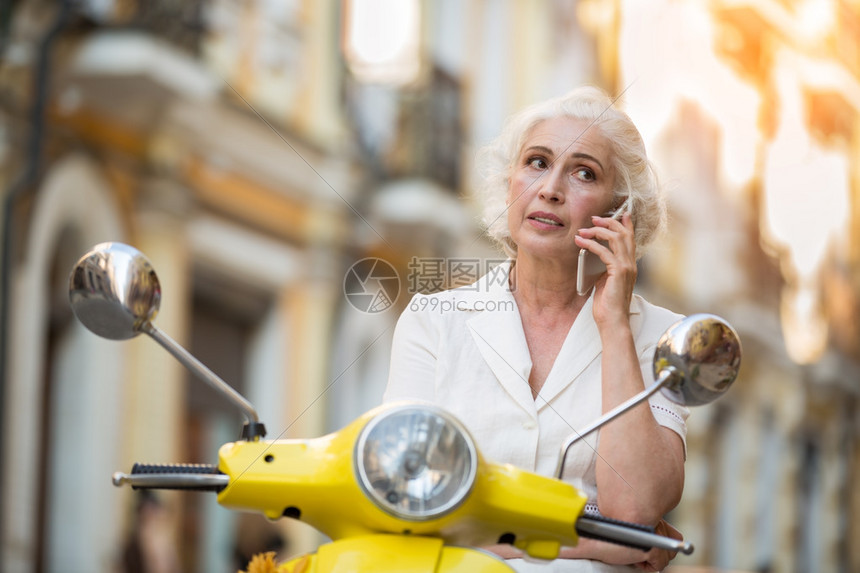 滑板车上的女人与电话成熟的女士拿着手机旅行时保持联系说图片