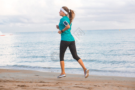 年轻适合可爱的运动女孩穿着运动服在早上日落时分在海滩上奔跑健身锻炼和健康的生活方式概念蓝天与云图片