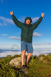 站在山顶的年轻人在日出时举起拇指表现出胜利情绪图片