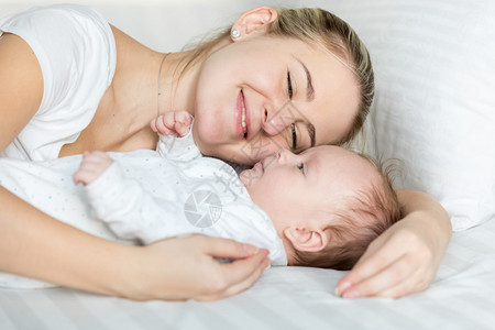 美丽微笑的女人抱着她可爱的婴儿躺在肖像图片