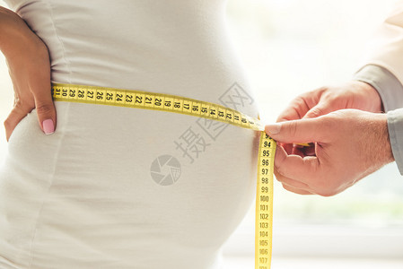 美丽的怀孕年轻女子和医生正在测量她的肚图片
