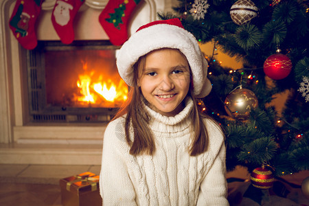 坐在房子里燃烧的壁炉边上坐着穿着圣诞老人帽子的欢图片