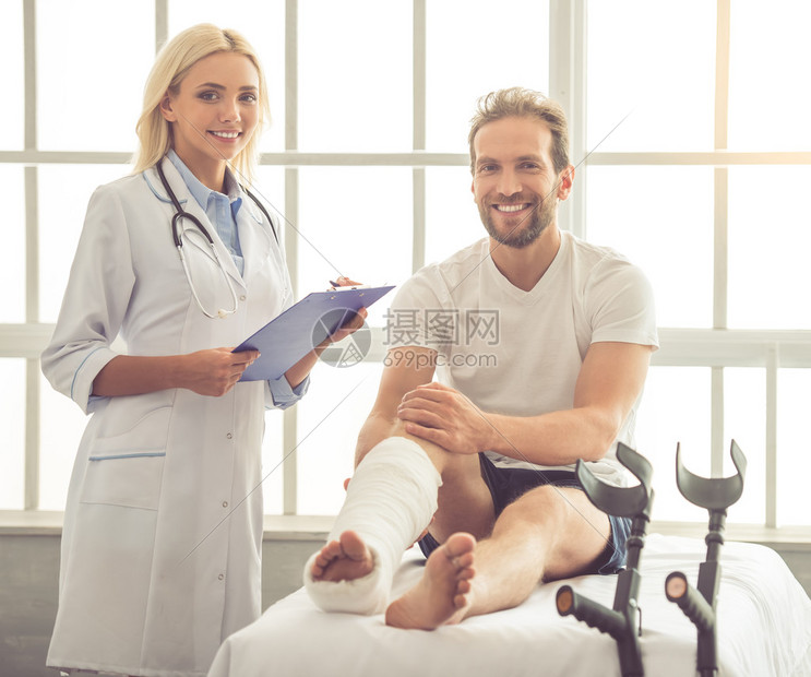 漂亮的女医生在她的办公室工作时正在听英俊的断腿病人做笔记两人都看图片