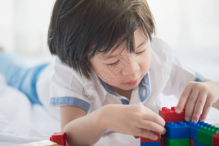 小亚洲儿童在白床上玩花样多彩的建筑块左图片