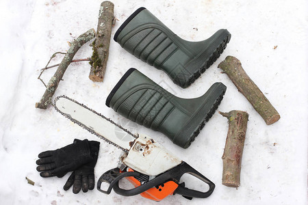 雪地背景上电锯手套靴子和原木的组合图片