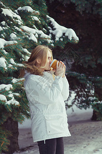 穿着白夹克的金发年轻女子在雪覆盖树木的背图片