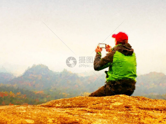 水彩色的油漆效果男人在岩石帝国高峰用智能手机拍照忧郁雾的风景图片
