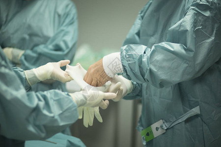 医院手术的外科医生在手术室急诊室的手术室中戴上无菌制服背景图片
