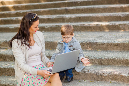 妈带着儿子和笔记本电脑在公园的楼梯上母子学习图片