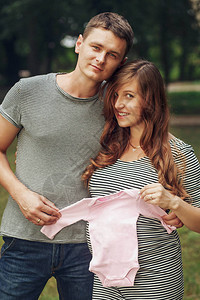 可爱的年轻已婚夫妇怀孕的妻子和为女婴带小粉红衣服的强健新郎图片