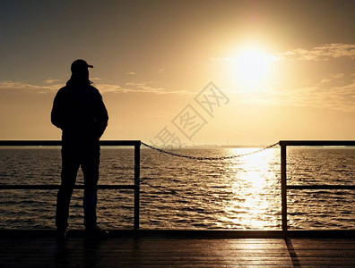 码头板上的成年高个子男在海面上望向太阳的清晨图片