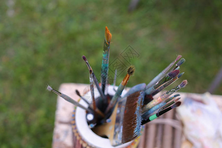 照片显示了用彩色铅笔和其他艺术品站在露天公园灰色桌子上的油和丙烯酸涂料的薄而厚的刷子艺术材图片
