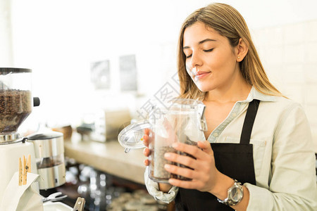 可爱的年轻女咖啡家在咖啡店里闻着咖啡谷物的味道图片