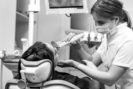 牙医用紫外线补牙的女患者的黑白特写视图医生正透过面罩微笑图片