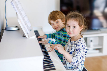 两个小孩女和男孩在客厅或音乐学校弹钢琴学龄前儿童在学习演奏乐器时获得乐趣教图片