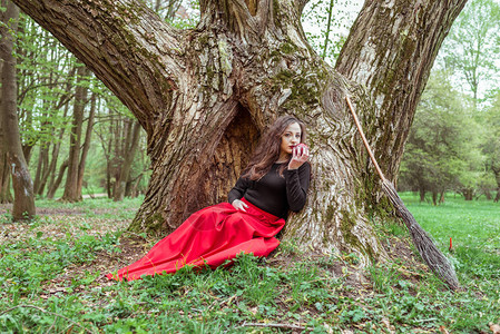 穿着红礼服的神秘巫婆坐在树下在春图片