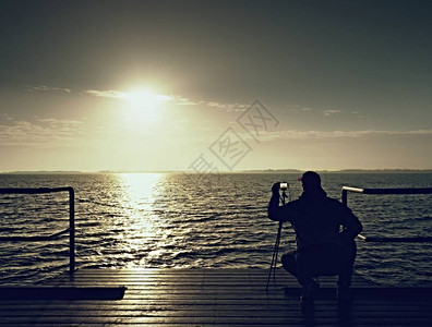 唯美梦幻用三脚架上的相机弯腰驼背的艺术家照片在摩尔扶手上的游客在海面上到早晨的地平线拍照游客在平滑的海平背景