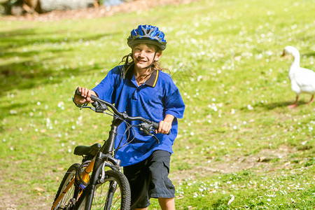 在自然公园背景下骑自行车的快乐青春期前男孩图片