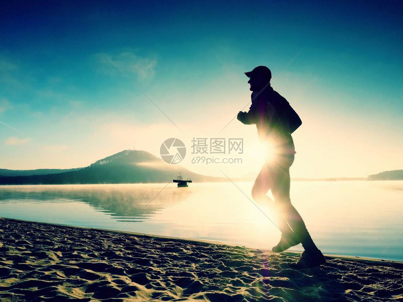 日出时在湖滩上奔跑的运动活跃男子的剪影健康的生活方式独自在早晨海滩锻炼的图片