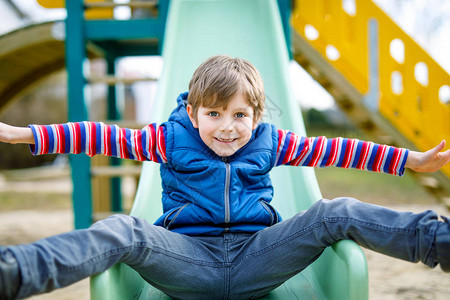 快乐的金发小男孩在户外操场上玩得开心滑有趣快乐的孩子微笑着爬上幻灯片夏季春季和秋季休闲活动的孩子穿着五颜六图片