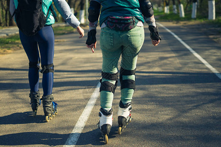 两个穿溜冰鞋的女孩骑着一条路走在彼此旁边的路上运动女图片