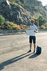 带着白空纸板牌标志的蓝背包带蓝色快乐的男人在日落或图片