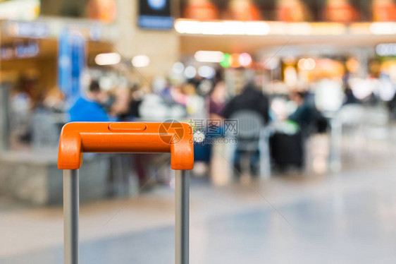 橙色手提箱在背景中与拥挤的机场咖啡厅关上门图片