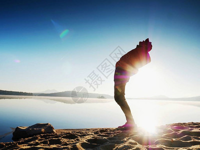 运动员男子向后弯腰在晨练和湖滩上慢跑时弯曲和伸展背部肌肉早上日出时在海上运动后图片