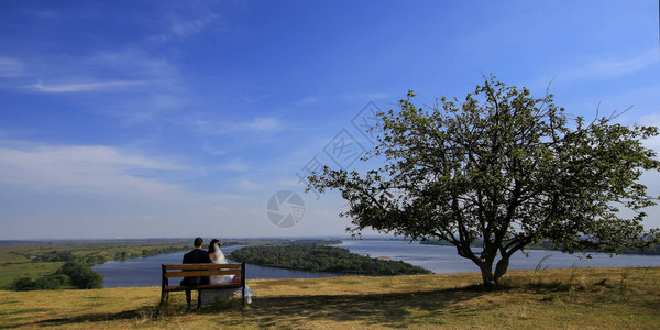 年轻的结婚浪漫情侣坐在户外的木板凳上以自然背景横向照片为图片