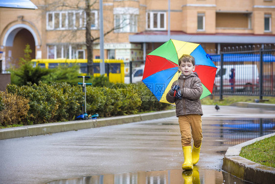 小男孩在多雨的夏日公园玩耍带着五颜六色的彩虹伞防水外套和靴子的孩子在雨中跳进水坑和泥泞中孩子在秋季淋浴间散步任何天气都可以图片