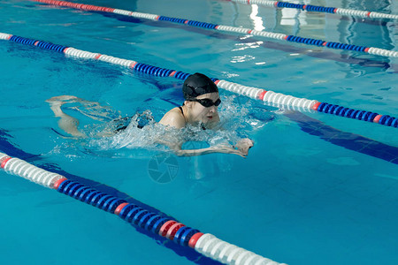 年轻女子在护目镜和帽在蓝色的水室内比赛池游泳蛙泳描边样式图片