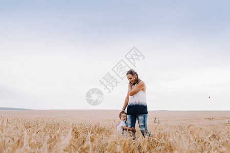 美丽的母亲和年轻的儿子在小麦田中走来图片