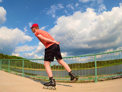 身穿红色t恤和黑色裤子的直排轮滑运动员在桥上滑冰的后视图在湖桥上光滑的混凝土地面上进行户外直排轮滑穿四轮靴图片