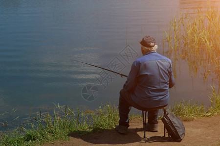 拿着鱼竿钓鱼的渔夫坐在河边阳光图片