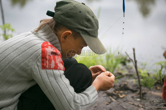 男孩在钓鱼衣服上的鱼饵上钩鱼竿图片