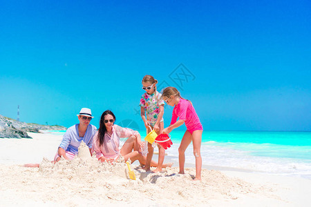 做在热带海滩沙子城堡的两个小孩的家庭图片