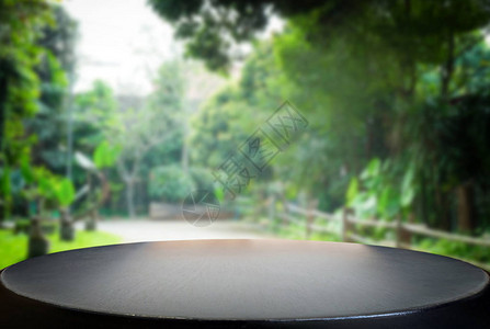 选中的空焦距黑木桌和绿色花园或森林模糊背景图片