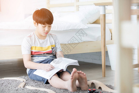 快乐的亚洲男孩在白床附近阅读故事书早晨图片