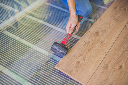 男子在温暖的薄膜地板上安装新的木质复合地板复合地板下的红图片