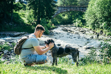 带着背包的年轻强健男子与狗在山河附图片