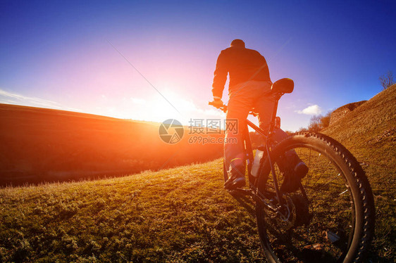 在日出时与阳光和蓝天空对立的山上自行车站立的骑手低角度视图闪烁季节极图片