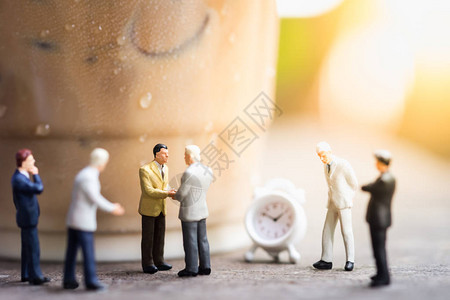 一群商人微型人物在靠近塑料杯的木桌上见面并握手图片