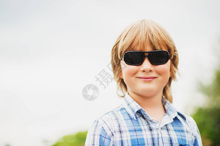 身戴太阳眼镜和蓝格子衬衫的6岁男孩在背景图片