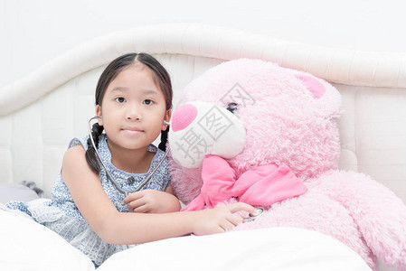 和大粉红泰迪熊在床上玩听诊器快乐的概念图片