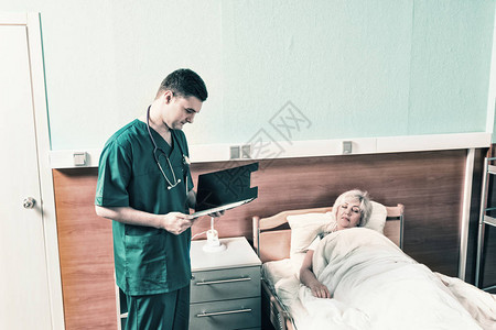 脖子上挂着电话内窥镜的年轻医生看着躺在病房床上的女病人的分析数图片
