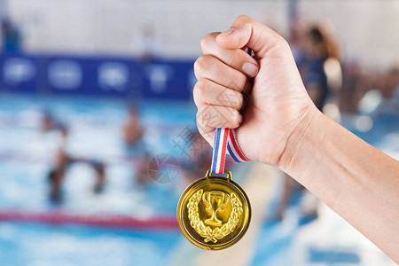 几个亚西人拿着金牌身着游泳池和游泳比赛的模糊背景图片