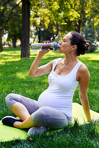 坐在瑜伽垫子上的有色相貌的运动型孕妇饮图片