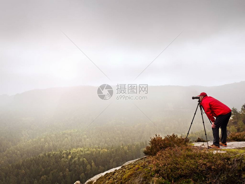 调查dslr数码相机取景器的摄影师站在三脚架上艺术家拍摄山区和多云的景观男人在拍摄自然照片时检查屏幕上的照片他的图片